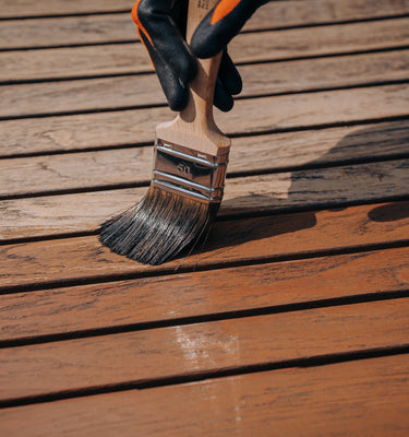 Pflege von Terrassendielen aus Holz mit einem Pinsel und schützendem Remmers Gartenholz-Öl.