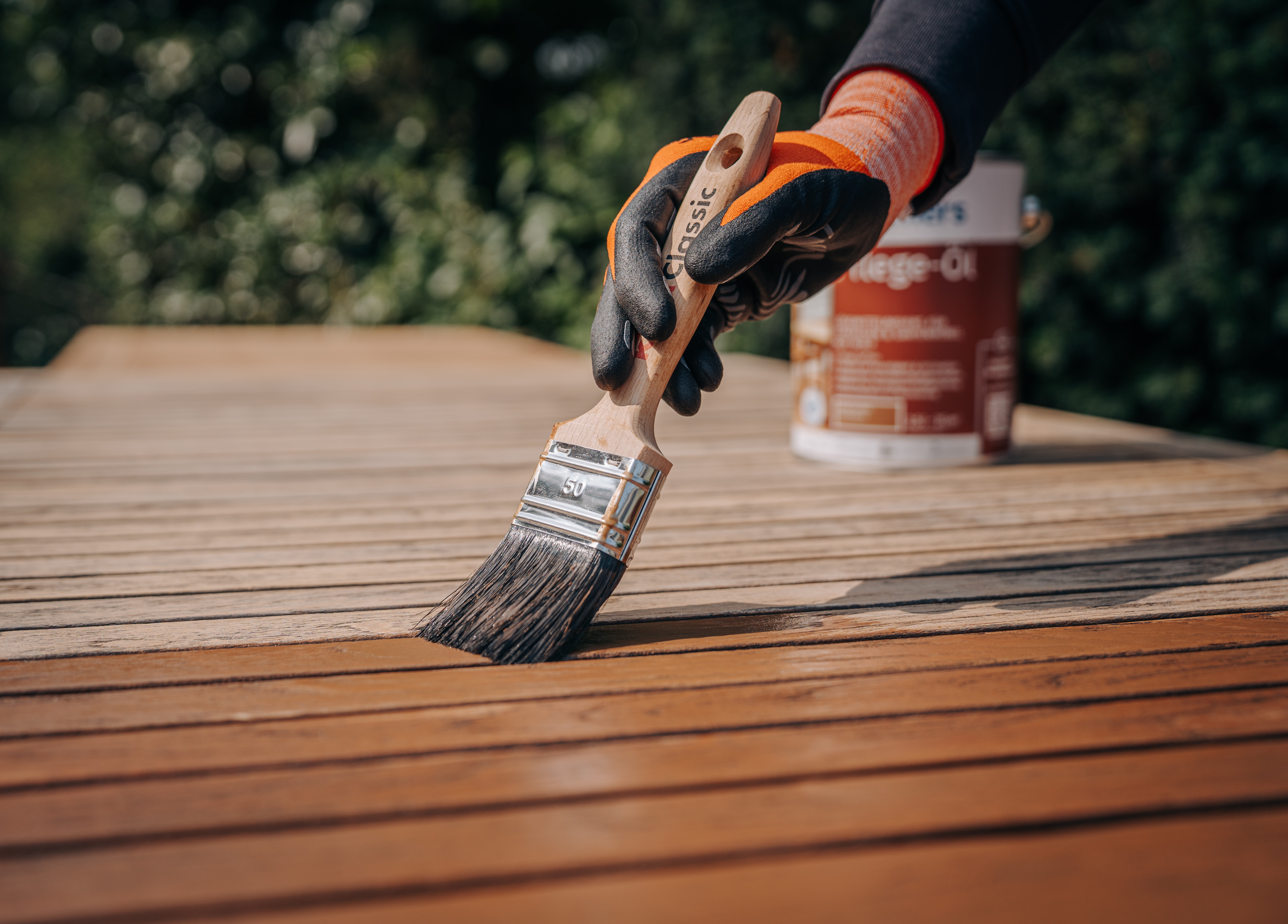 Ein Gartentisch aus Holz wird mit einem Pinsel und Remmers Pflege-Öl für neuen Glanz und Schutz gestrichen.