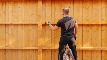 Eine Holzwand wird mit einem Pinsel und Remmers HK-Lasur für langlebigen Wetterschutz gestrichen.