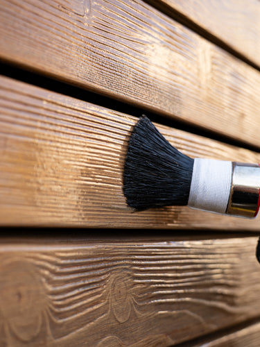 Pflege einer Holzwand mit Remmers Holzschutz-Creme und einem Lasurpinsel